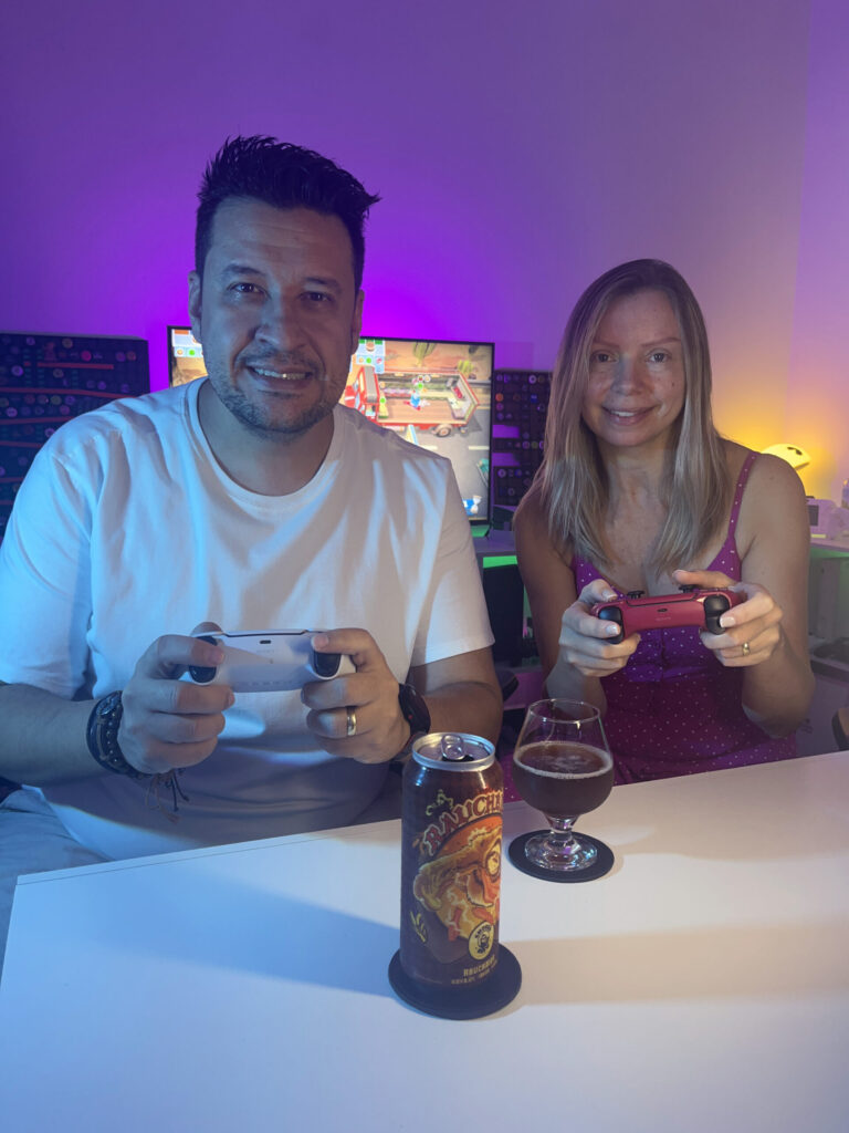 Cerveja escura estilo Rauchbier ao lado de gameplay cooperativo de Overcooked no PS5 com dois controles na mesa.