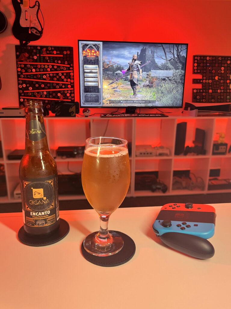 Cerveja Pilsen dourada ao lado de tela inicial de Diablo II Resurrected com personagem Bruxo selecionado.
