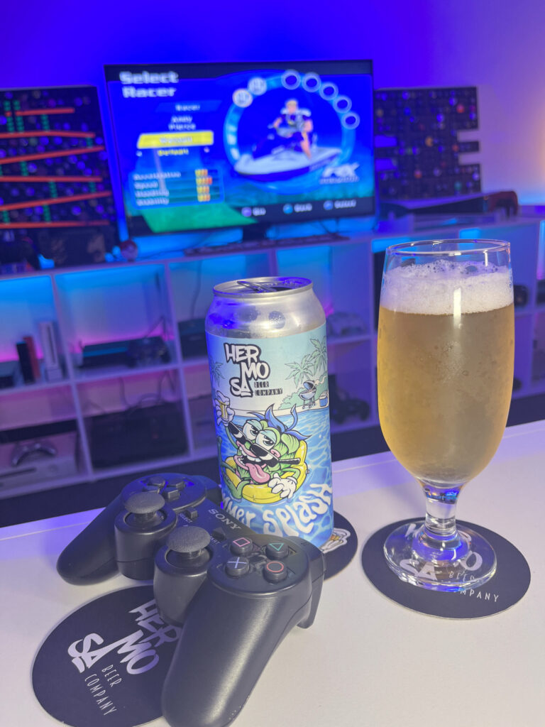 Cerveja New Zealand Pilsner amarelo ouro ao lado de Splashdown no PlayStation 2 em clima de verão.