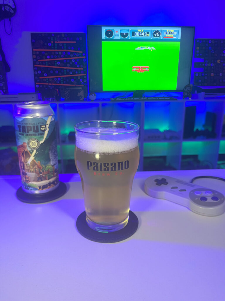 Cerveja clara e translúcida ao lado de gameplay de Pilotwings no Super Nintendo com cenário aéreo retrô.