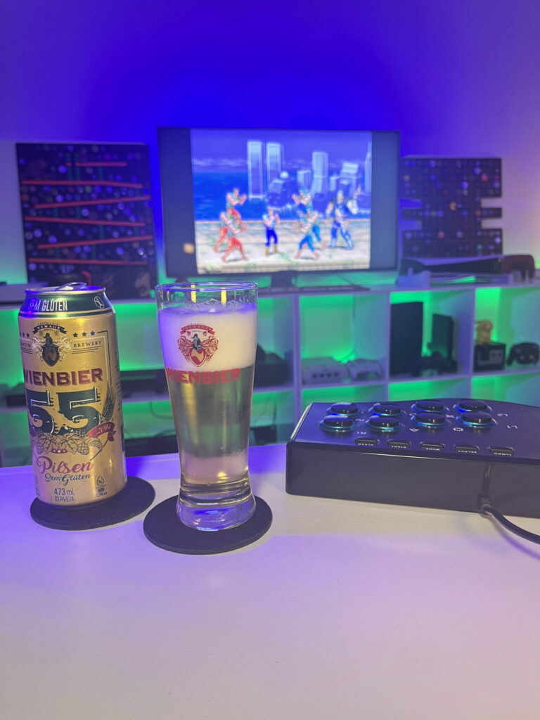 Cerveja Pilsen sem glúten amarelo claro ao lado de Cadillacs and Dinosaurs no Arcade em clima retrô.