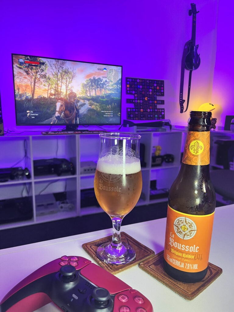 Belgian Golden Strong Ale La Boussole, da Caixa da Alegria, ao lado de The Witcher 3 Wild Hunt Remastered no PS5.