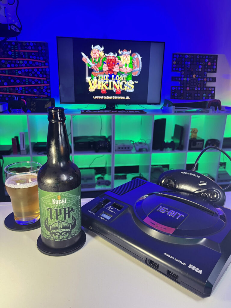 Session IPA dourada e levemente turva, da Kurši Cervejaria, ao lado de The Lost Vikings no Mega Drive.