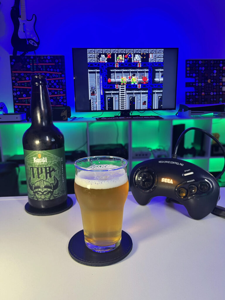 Session IPA dourada e levemente turva, da Kurši Cervejaria, ao lado de The Lost Vikings no Mega Drive.