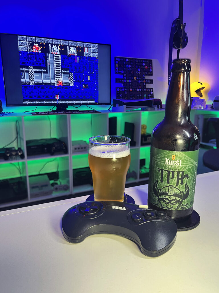 Session IPA dourada e levemente turva, da Kurši Cervejaria, ao lado de The Lost Vikings no Mega Drive.