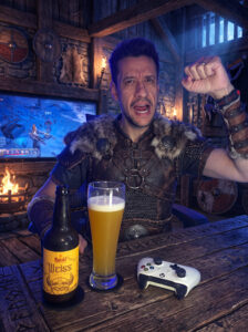 Cerveja Weiss amarelo palha ao lado de Vikings: Wolves of Midgard no Xbox One em clima de taverna viking.