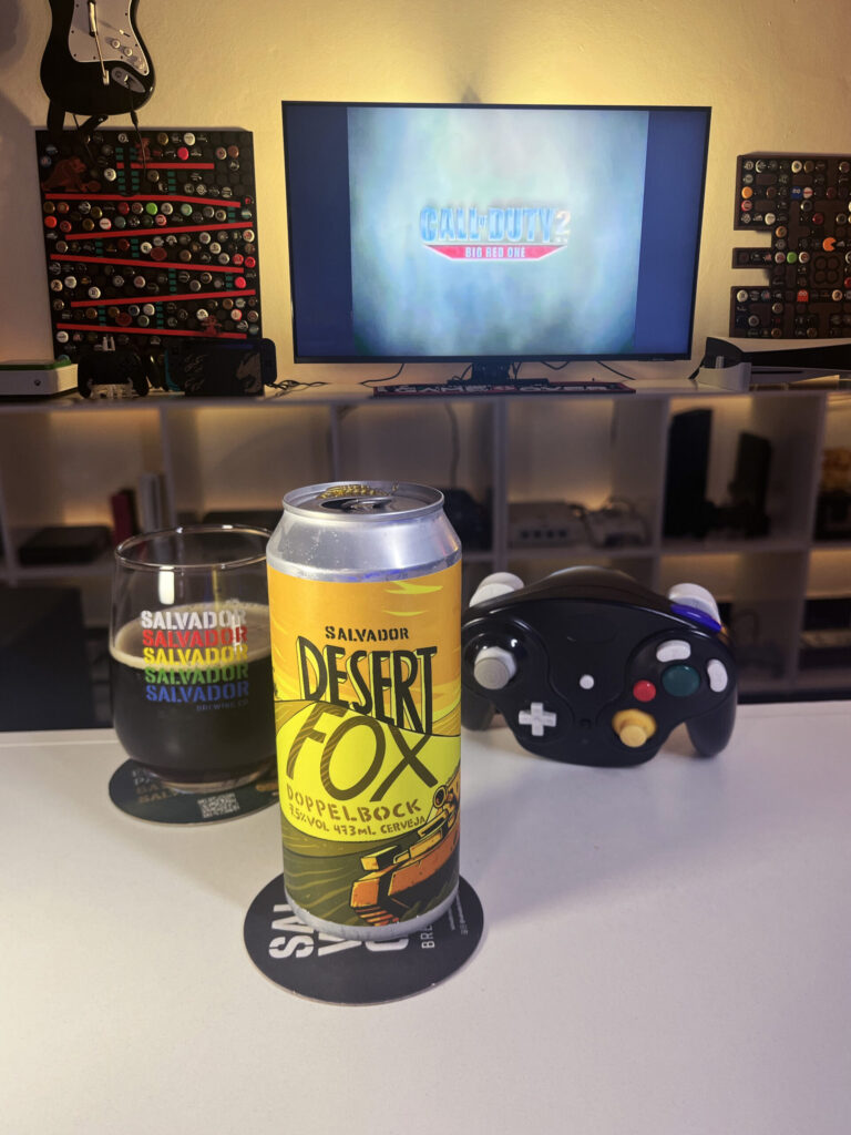 Cerveja Desert Fox cor de carvalho com nuances rubis, ao lado de Call of Duty 2: Big Red One no GameCube.